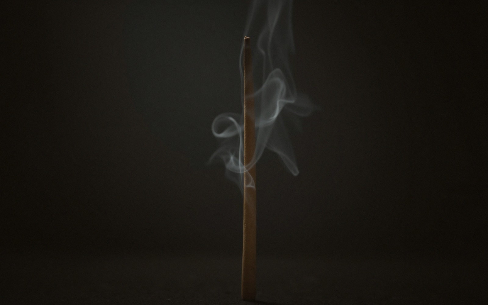 Smoke curls upward from a burning incense stick against a dark background