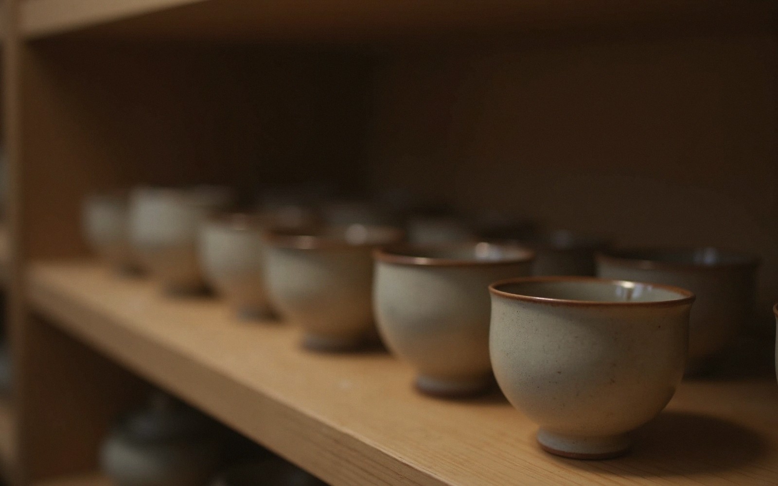 Rows of glazed ceramic teacups lined up on a wooden shelf