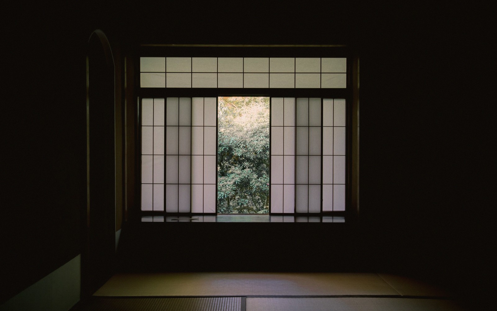 Sliding paper shoji screens open to a green garden view in a dim tatami room