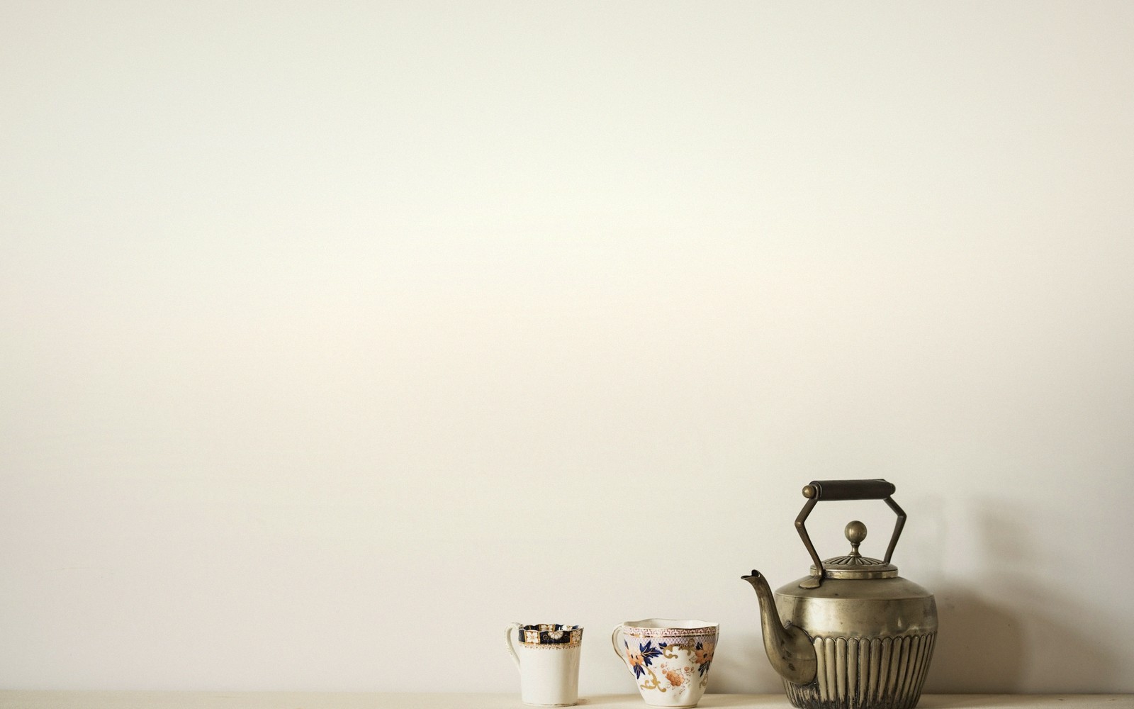 A metal kettle beside two small patterned teacups on a shelf